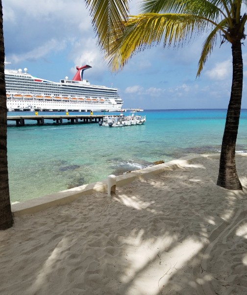 Carnival cruise ship docked beside a tropical beach with turquoise water.